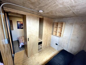 Una habitación pequeña con una cama, una estantería de madera y una puerta que da a otra habitación.