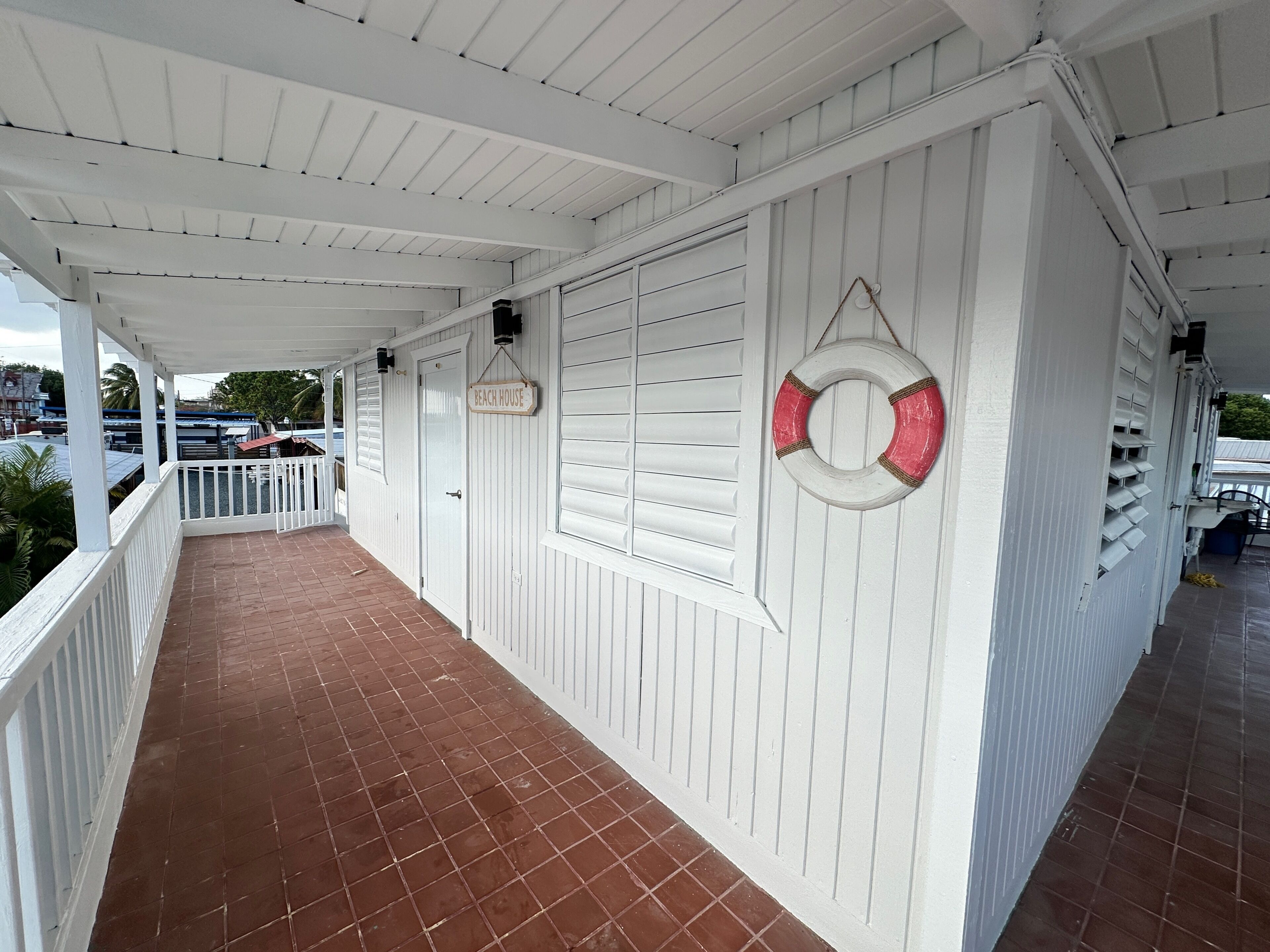 A covered porch with a tiled floor, white railings, and a lifebuoy hanging on the wall.