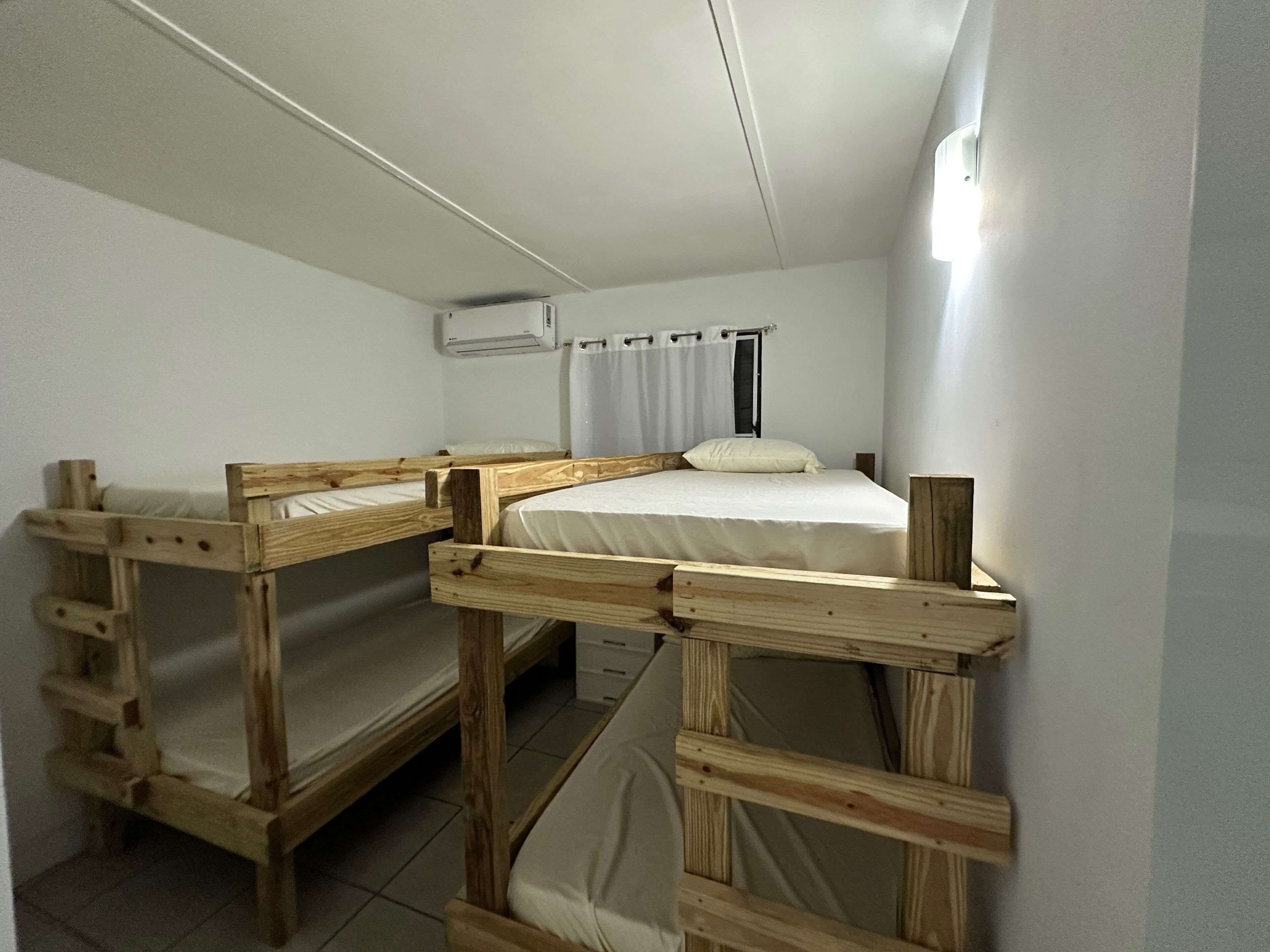 Ein Schlafsaalzimmer mit zwei Etagenbetten, einem Deckenventilator und einer Klimaanlage.
