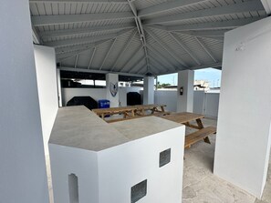 An outdoor covered patio area with picnic tables and a barbecue grill. - Perfect 7-bedroom building with AC, private pool, generator, cistern in Combate (Combate)