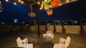 Zona esterna con tavoli e sedie, fioriere pensili e vista sulla città di notte.