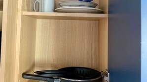 Un mobiletto in legno con una padella nera, un piatto bianco e una tazza blu sullo scaffale inferiore.