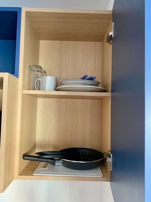 Ein Holzkabinett mit einer schwarzen Bratpfanne, einem weißen Teller und einer blauen Tasse auf der unteren Ablagefläche.