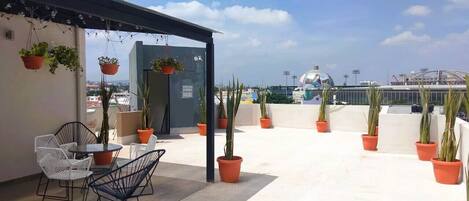 A rooftop terrace with outdoor seating, potted plants, and a view of the cityscape.