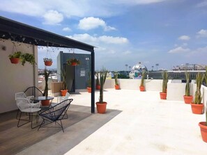 Eine Dachterrasse mit Sitzgelegenheiten im Freien, Topfpflanzen und Blick auf die Stadtlandschaft.