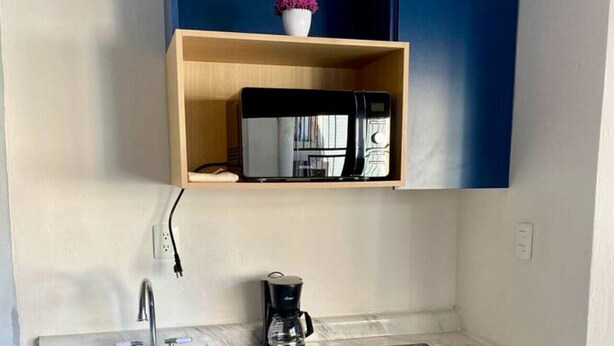 Un angolo cottura funzionale con microonde integrato, macchina del caffè e piccolo frigorifero.