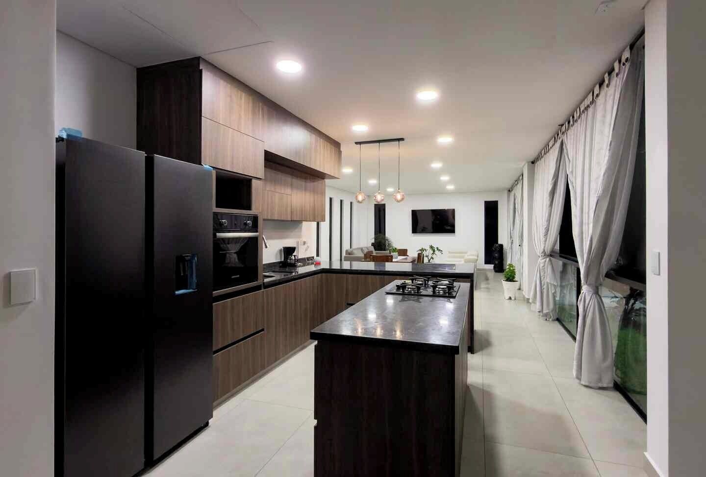 Una cocina moderna con gabinetes de madera oscura, un refrigerador de acero inoxidable y una isla central con estufa a gas.