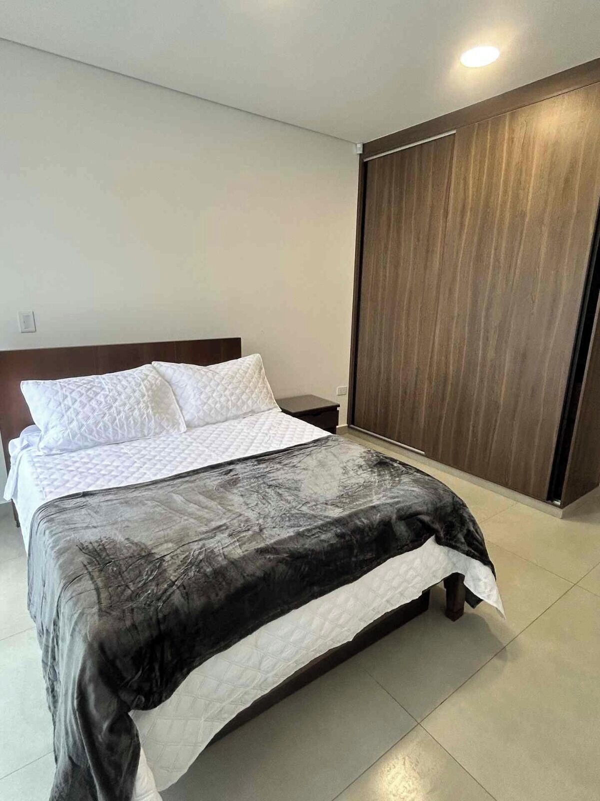 A bedroom with a bed, a nightstand, a wooden wardrobe, and a ceiling light.