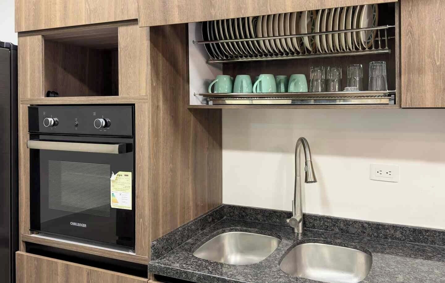 A kitchen with a built-in oven, a stainless steel sink, and a dish rack above the countertop.