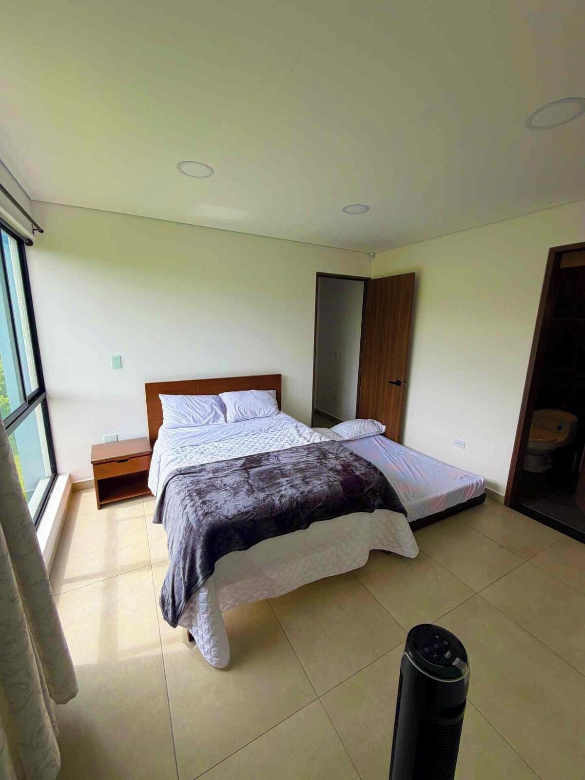 A bedroom with a bed, a nightstand, a wardrobe, and a bathroom visible through an open door.