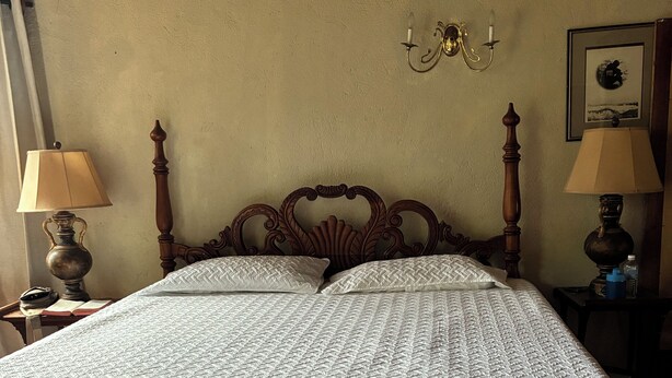 Una cama con estructura de madera y colcha estampada, flanqueada por dos mesitas de noche con lámparas, frente a una pared con textura.