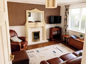 Ein Wohnzimmer mit Ledersofas, einem Kamin, einem Fernseher und einem Bücherregal.