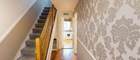 A hallway with carpeted stairs, a washing machine, and patterned wallpaper.