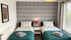 Quarto duplo com duas camas, um radiador, um quadro na parede e uma janela com cortinas.