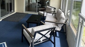 Eine sonnendurchflutete Terrasse mit Deckenventilator, einer Couch, einem Tisch und Blick auf einen Küchenbereich durch Glasüren.