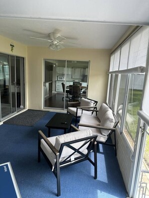 A sunlit patio with a ceiling fan, a sofa, a table, and a view of a kitchen area through glass doors. - Palm Harbor Retreat  2BR / 2BA Home (Palm Harbor)