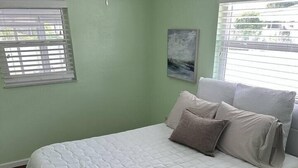 Ein Schlafzimmer mit einem Bett, einem Fenster mit Jalousien, einem Gemälde an der Wand und einem Teppich.