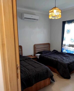 Une chambre avec deux lits, une tête de lit en bois, un luminaire suspendu et une fenêtre donnant sur un beau paysage.