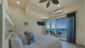 A bedroom with a bed, a flat-screen TV, a ceiling fan, and a view of the sea through a sliding glass door. - 4BR Oceanfront Home | Incredible Views & Private Pools (Isla Mujeres)