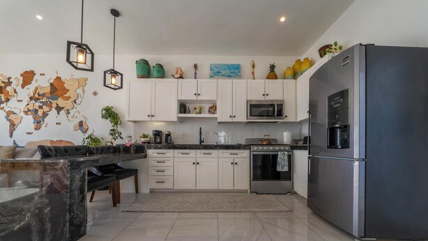 A modern kitchen with white cabinets, a black refrigerator, a microwave, and a stove. There are hanging lights and a world map on the wall. - 4BR Oceanfront Home | Incredible Views & Private Pools (Isla Mujeres)