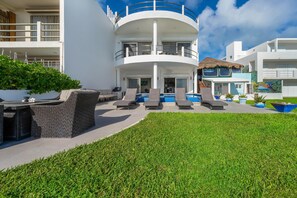 A modern multi-story building with a pool area, outdoor seating, and a well-maintained lawn. - 4BR Oceanfront Home | Incredible Views & Private Pools (Isla Mujeres)