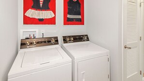 A laundry area with two white washing machines and two red and black wall art pieces. - Unobstructed Lake Erie Views — Sunrise from the Covered Front Porch (Lakeside Marblehead)