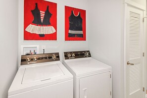 A laundry area with two white washing machines and two red and black wall art pieces. - Unobstructed Lake Erie Views — Sunrise from the Covered Front Porch (Lakeside Marblehead)