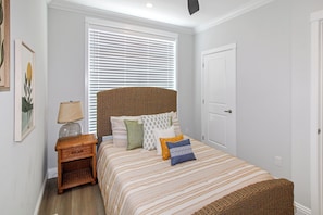 A bedroom with a bed, a nightstand, a lamp, a window with blinds, and a door.
