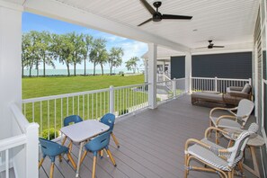 A covered outdoor area with a table and chairs, a ceiling fan, and a view of the ocean. - Unobstructed Lake Erie Views — Sunrise from the Covered Front Porch (Lakeside Marblehead)