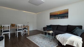 Ein modernes Wohnzimmer mit einem dunklen Sofa, einem Schachtisch und einem Gemälde, das einen Sonnenuntergang zeigt.
