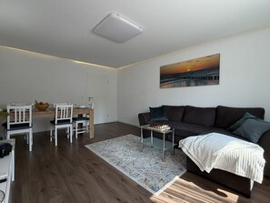 Ein modernes Wohnzimmer mit einem dunklen Sofa, einem Schachtisch und einem Gemälde, das einen Sonnenuntergang zeigt.