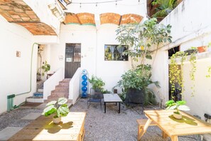 Une cour avec un escalier, une table, des chaises et diverses plantes en pot.