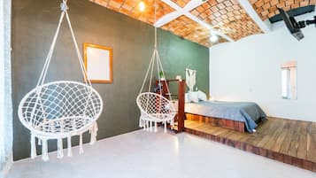Een slaapkamer met een bed, twee hangstoelen, een houten platform en een plafond van baksteen.