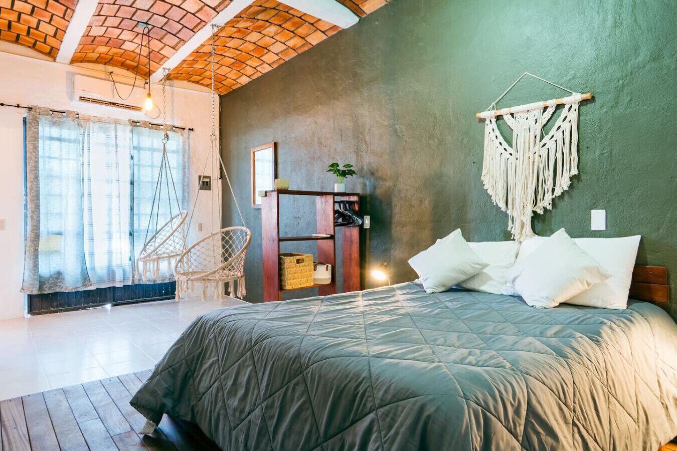 Une chambre avec un lit, un fauteuil suspendu, une étagère avec des paniers et une décoration murale en macramé.