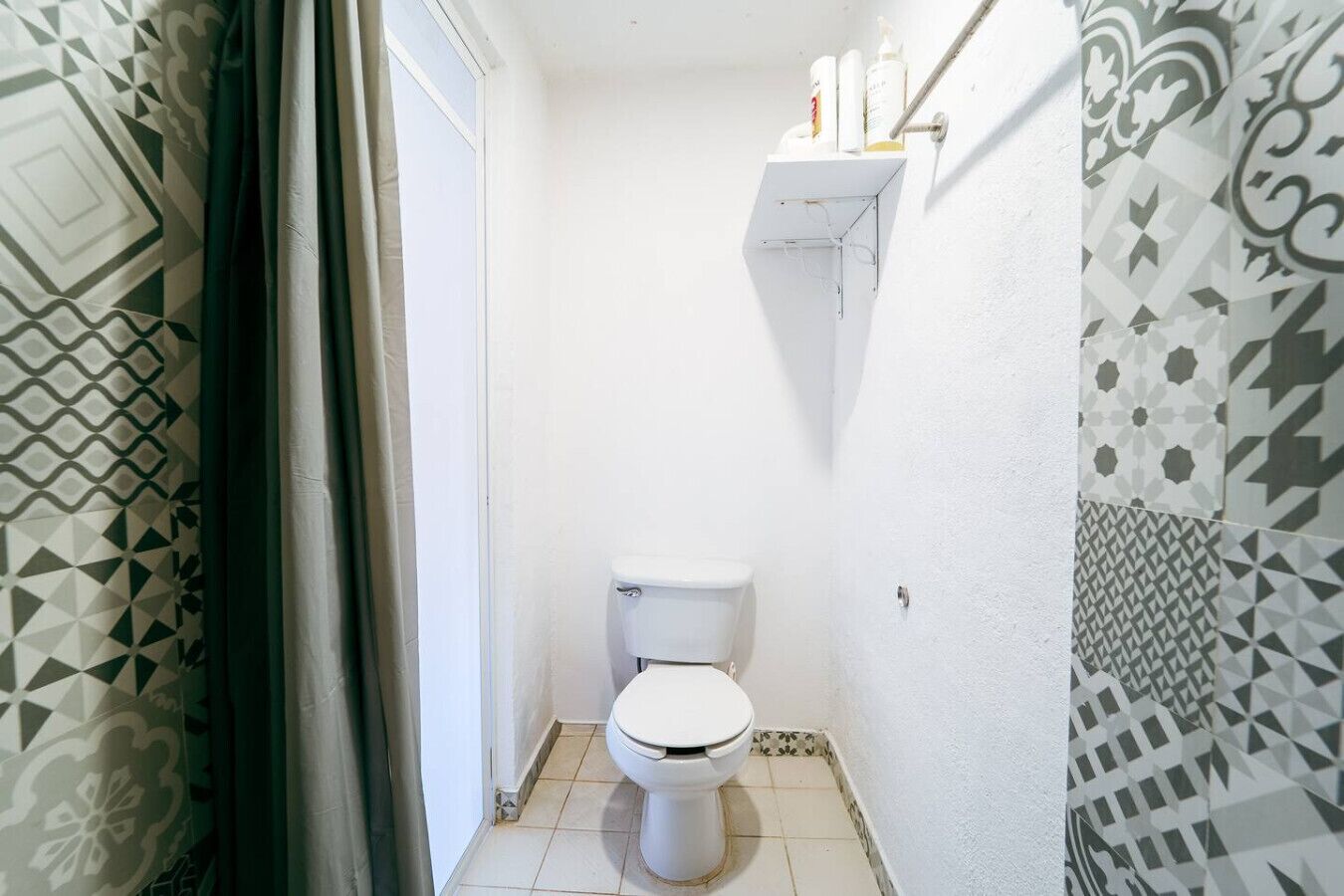 A small, narrow bathroom with a toilet, a shelf with toiletries, and patterned walls.