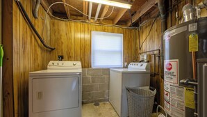A laundry room with two washers and dryers, a metal water heater, and a window with blinds. - Cozy 2-bedroom house. Office Space. Projector. Coffee Station included. (Cincinnati)