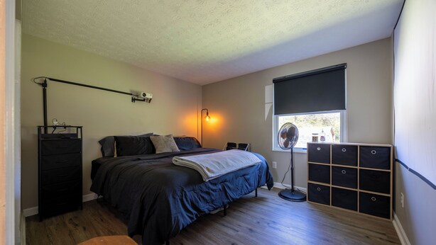 A bedroom with a bed, a desk, a chair, a dresser, a floor lamp, and a window with blinds. - Cozy 2-bedroom house. Office Space. Projector. Coffee Station included. (Cincinnati)