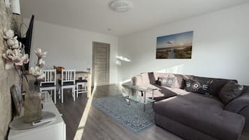 Ein modernes Wohnzimmer mit grauem Sofa, einem Glastisch und einem Essbereich mit weißen Stühlen.