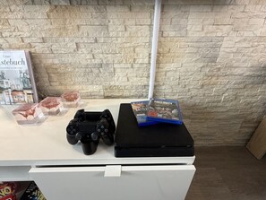 A gaming setup with a PlayStation controller and a game case on a white table against a stone wall backdrop.