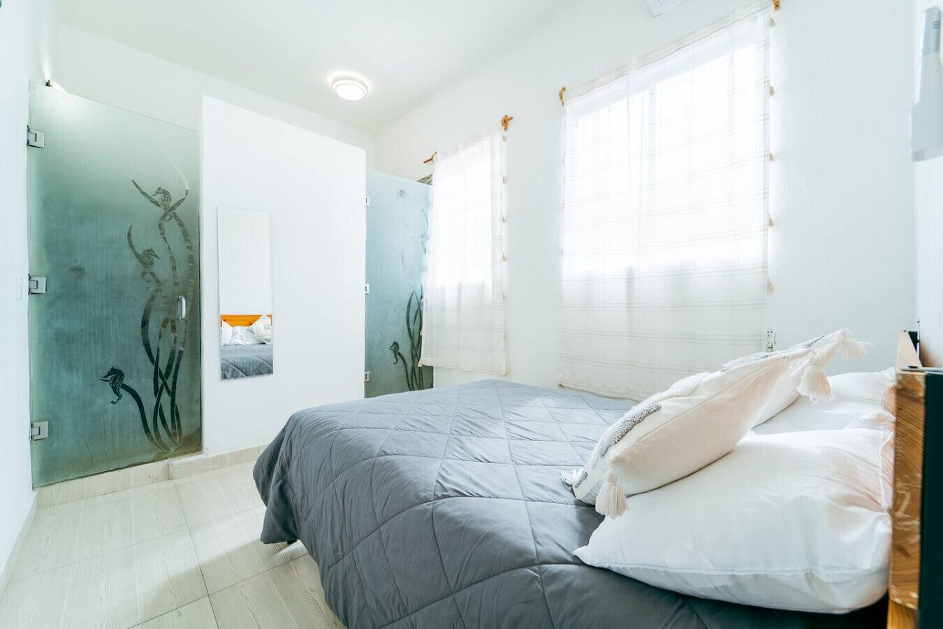 A bedroom with a bed, a mirror, and a window with curtains.