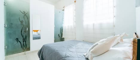 A bedroom with a bed, a mirror, and a window with curtains.