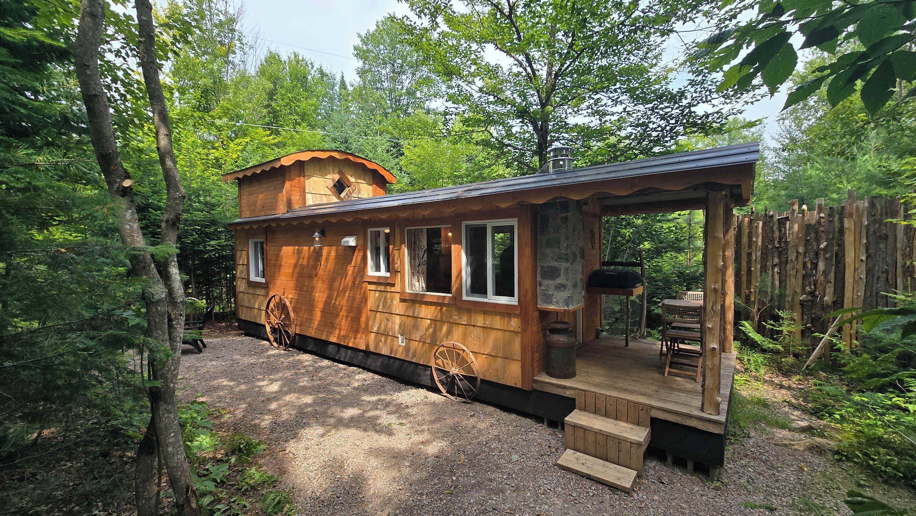 Une cabane en bois avec une véranda, une cheminée en pierre et une table à manger installée à l’extérieur.