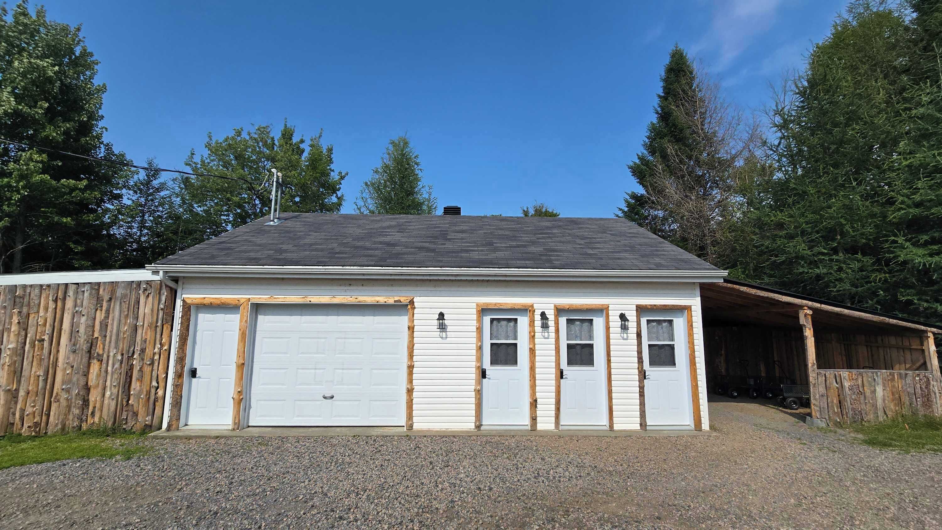 Un bâtiment à deux étages avec un garage, une façade en bois et une allée gravillonnée.