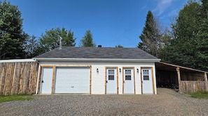 A two-story building with a garage, wooden exterior, and a gravel driveway. - Waterfront Glamping | La Nomade (Shannon)