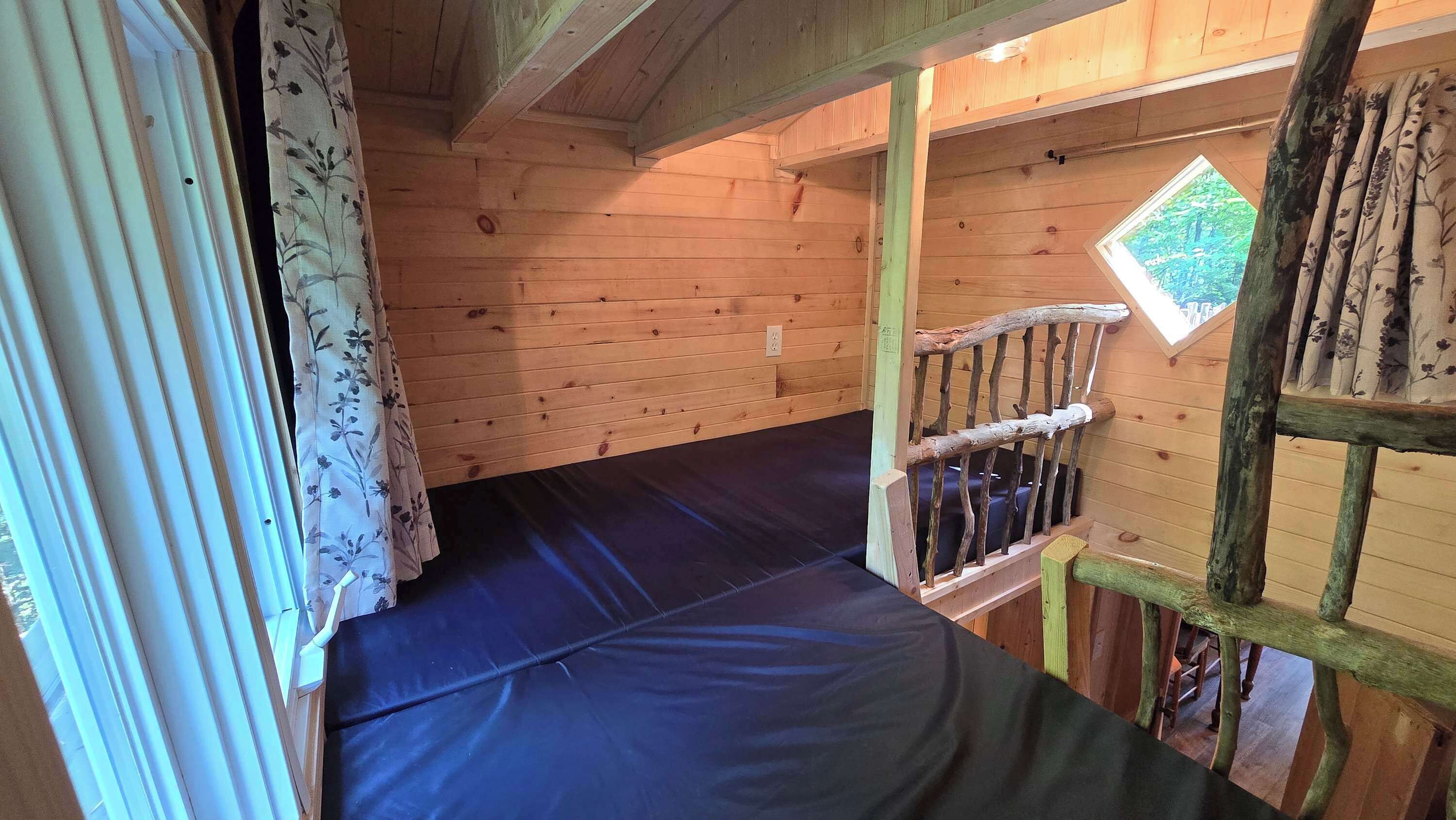 Une cabane en bois avec un lit superposé, une fenêtre donnant sur un paysage agréable et un escalier en bois.