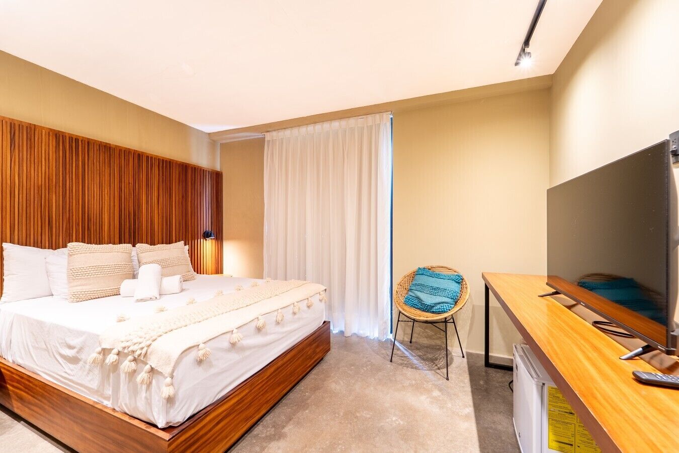 Une chambre d’hôtel avec une tête de lit en bois, un lit avec du linge de maison blanc, un bureau avec une télévision et une chaise.