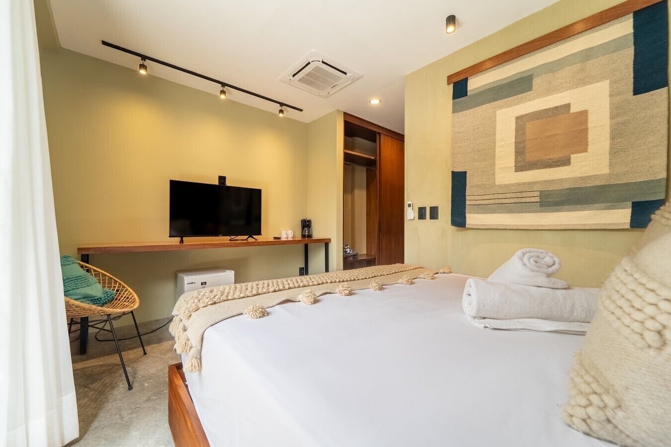A hotel room with a bed, a television, a desk, a chair, and a wall with a geometric patterned design.