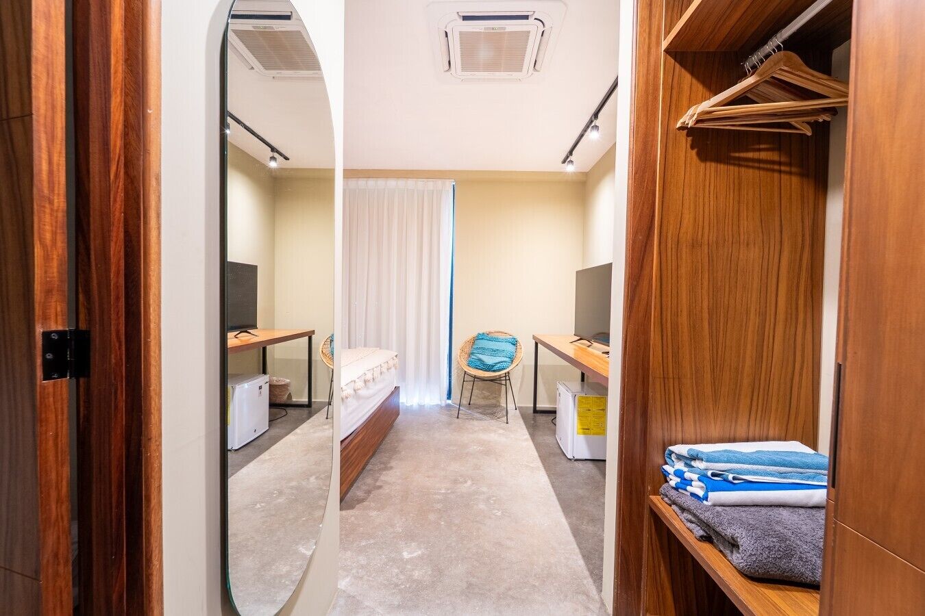 A narrow hallway leading to a bedroom with a bed, a desk, a chair, and a wardrobe.