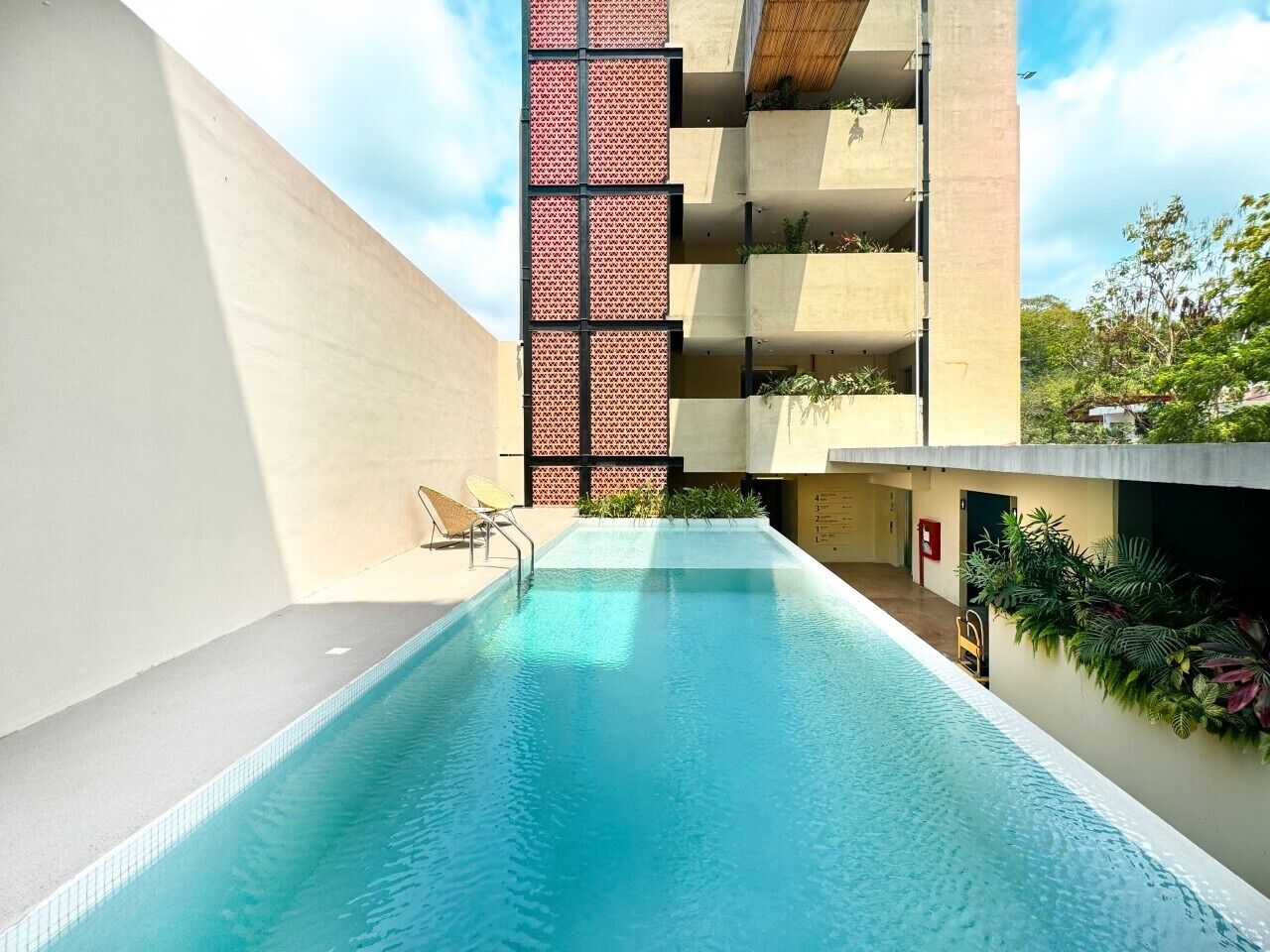 Ein Schwimmbecken mit Liege, umgeben von einem Gebäude mit Balkonen und Pflanzen.