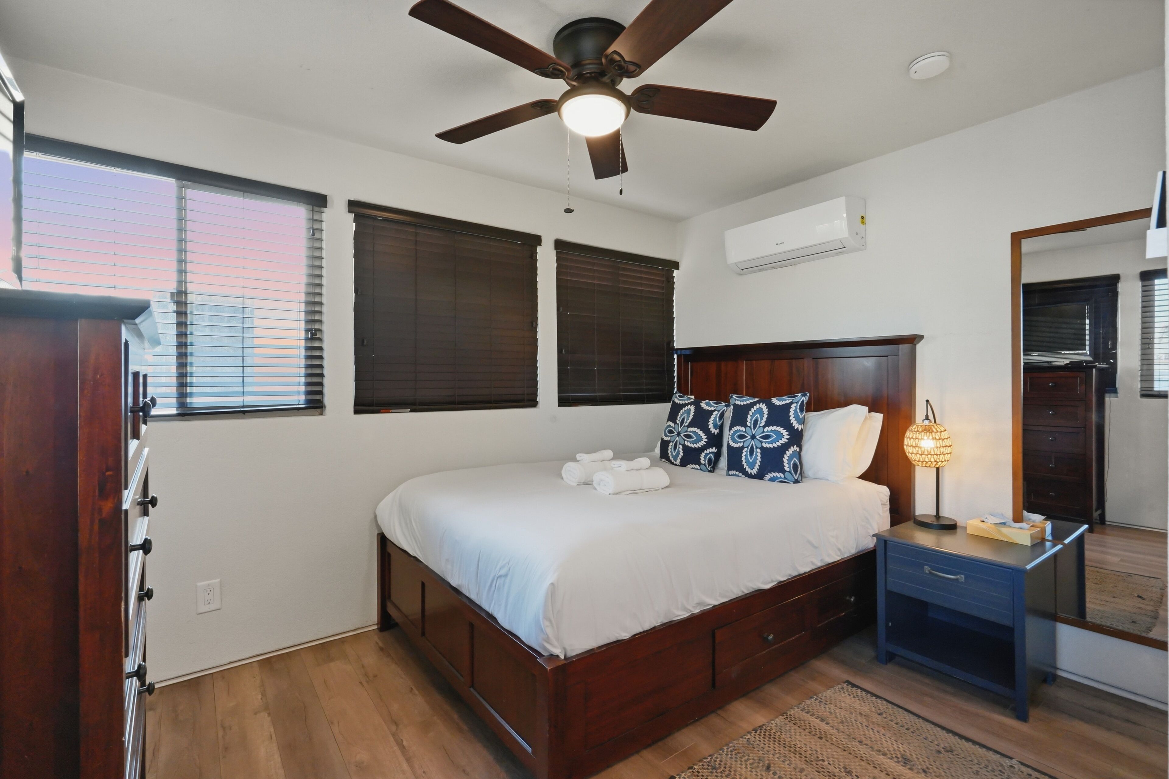 Quarto com cama, mesa de cabeceira, abajur e ventoinha no teto.